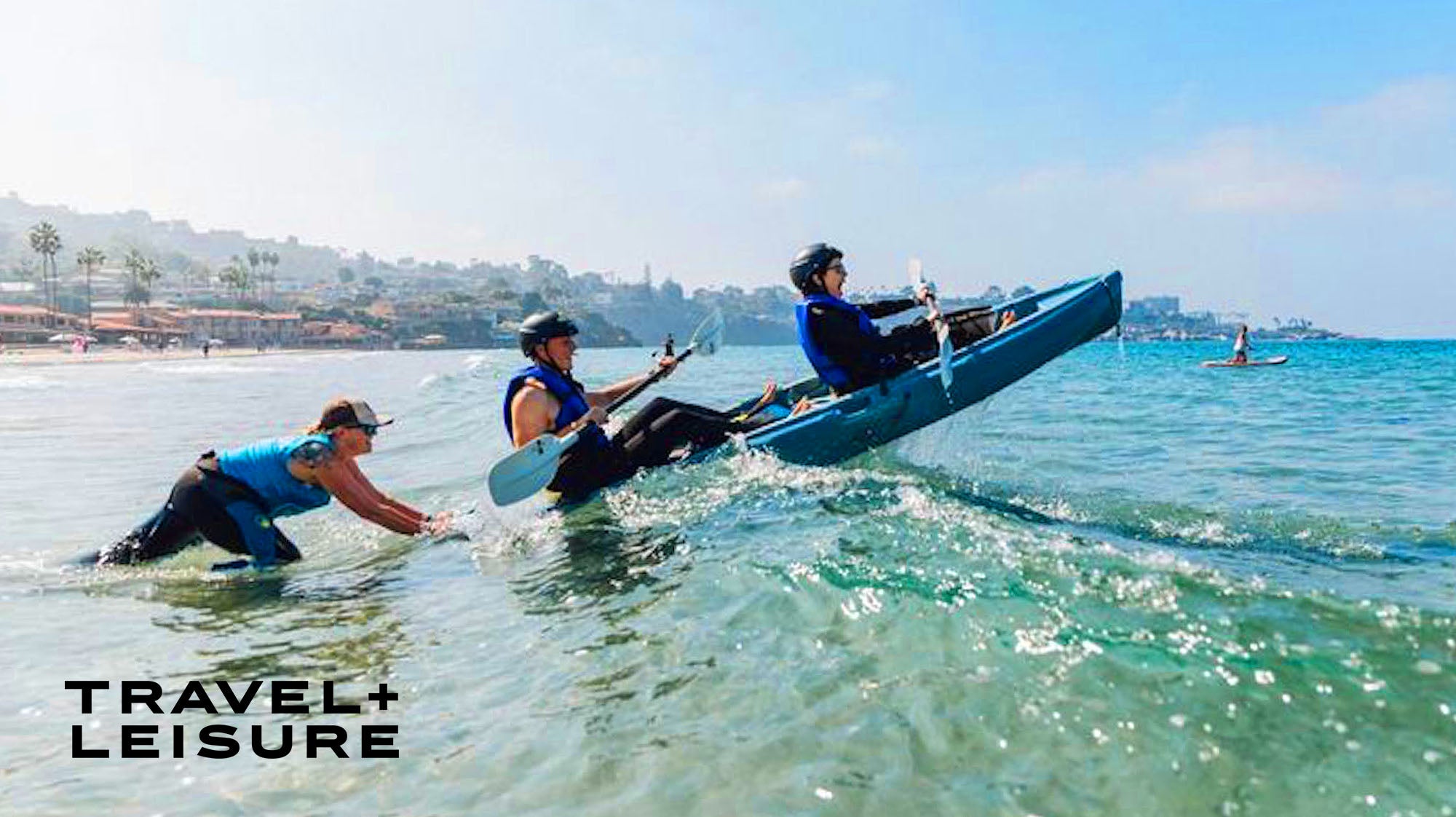 Two kayakers in the open ocean near the shore being pushed over the top of a wave by an Everyday California kayak tour guide in La Jolla.