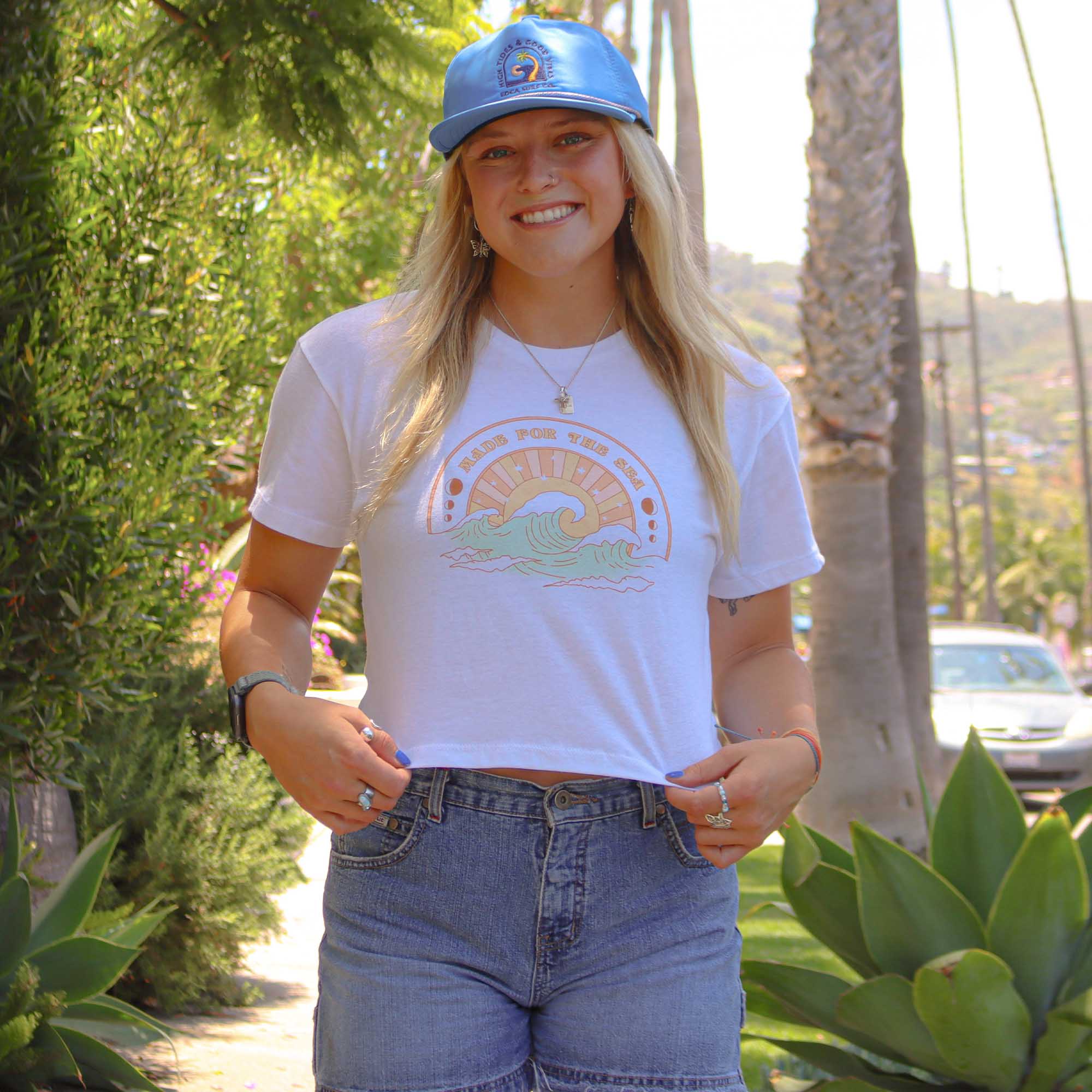 A model showcasing the Women's Tourmaline Crop Tee with "Made for the Sea" printed on the front above a design of a wave and sun